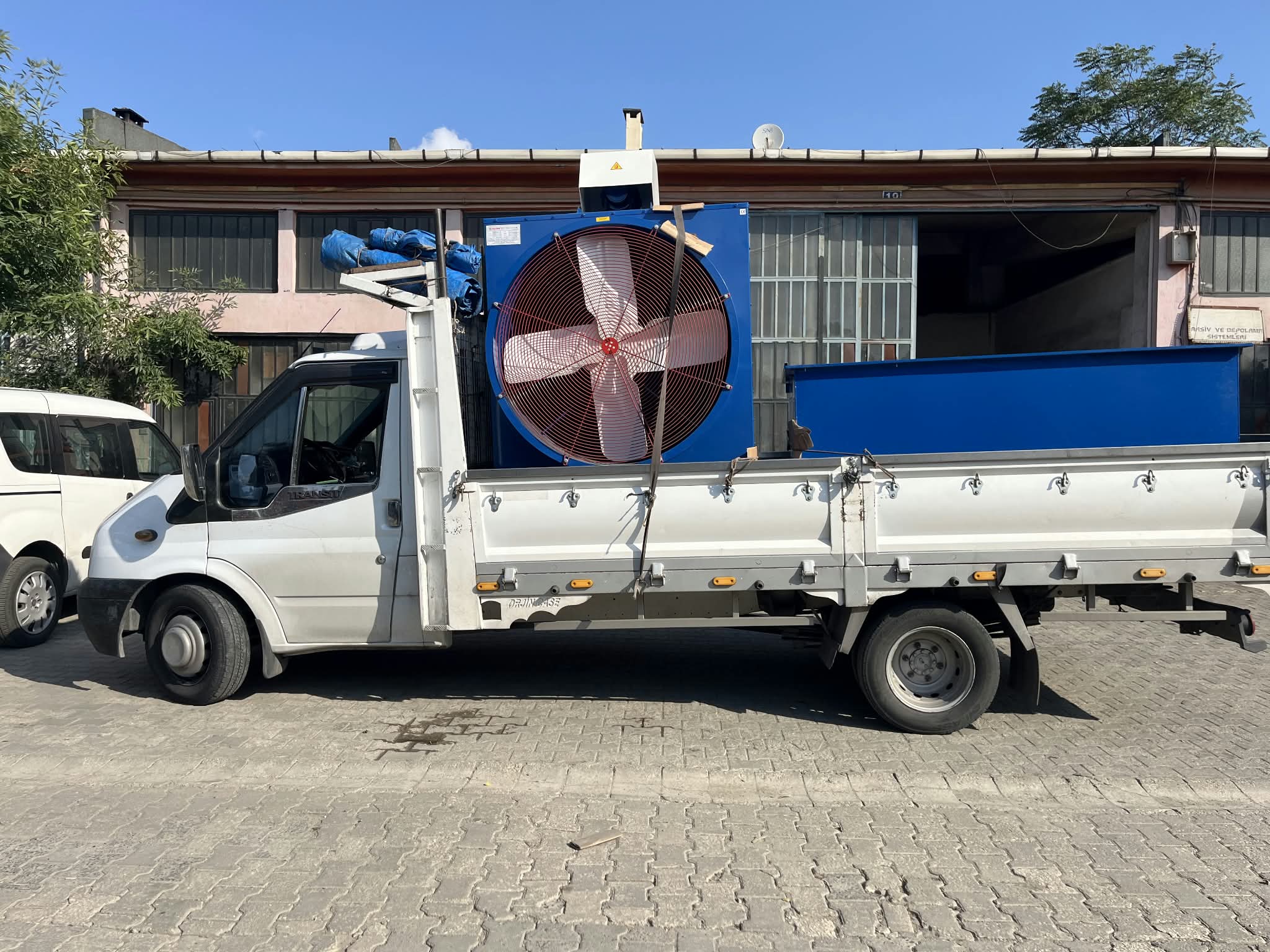 Kayışlarla sabitlenmiş ağır sanayi ekipmanı taşıyan açık kasa kamyonet yan görünüm